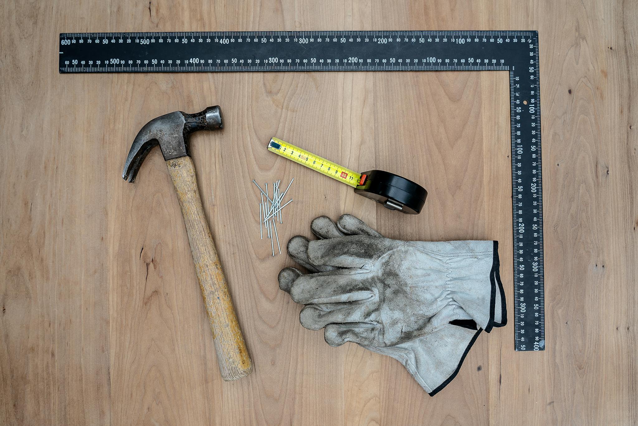 Flat lay of essential carpentry tools including a hammer, gloves, and more on a wooden surface.